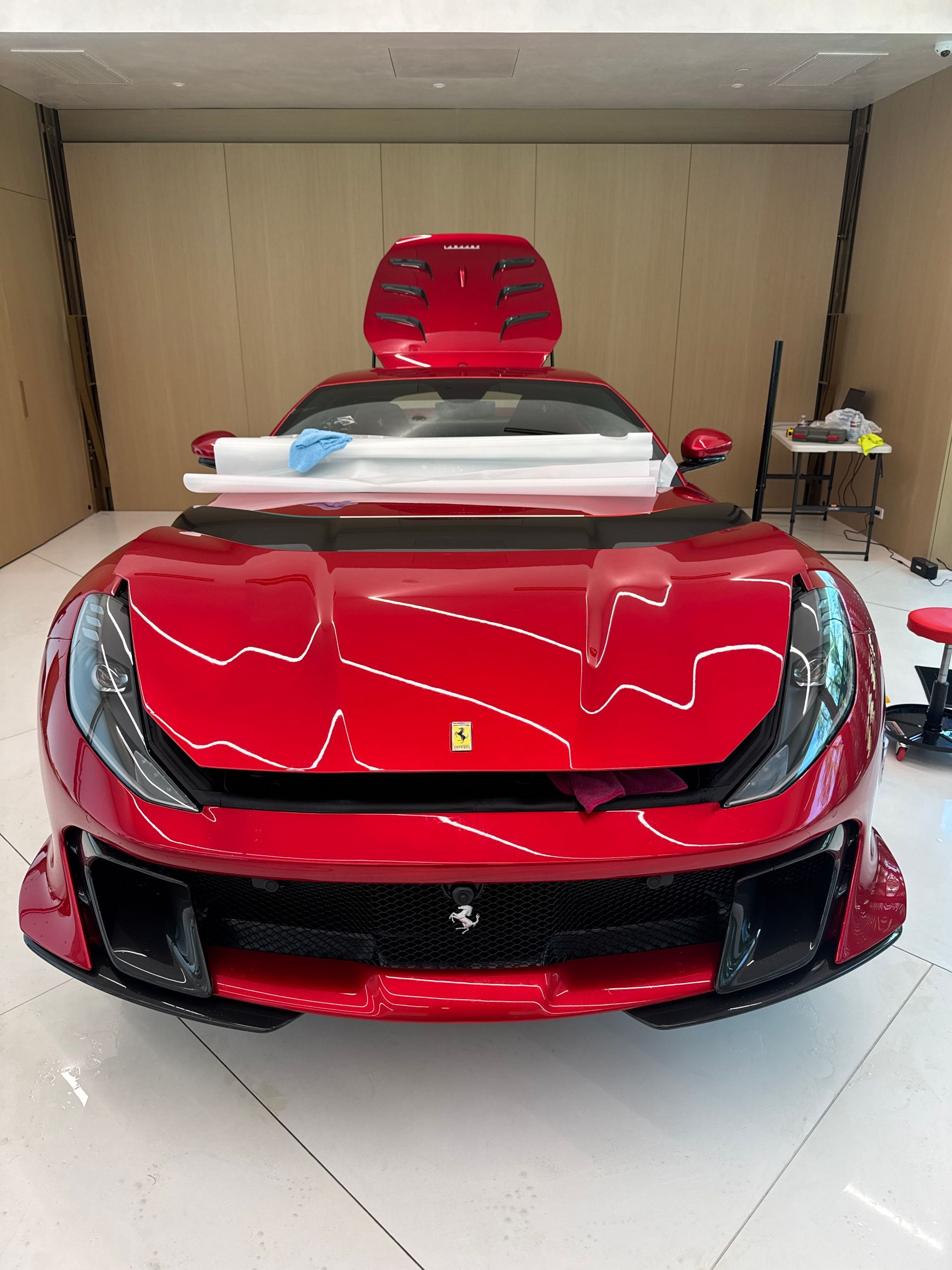 Red Ferrari with hood open, in a bright workshop, ready for detailing.