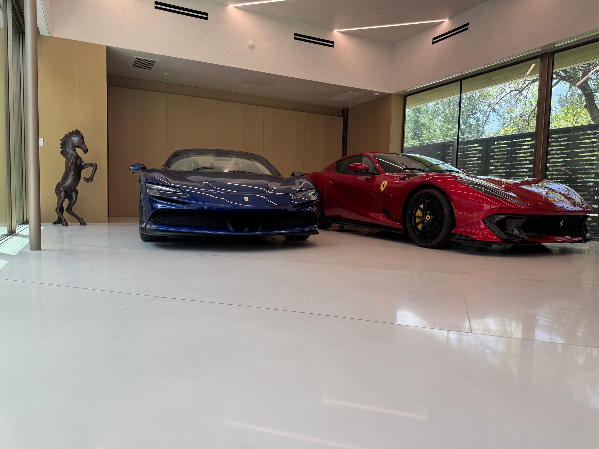 Two sports cars, one blue, one red, parked inside a garage with polished white floor.
