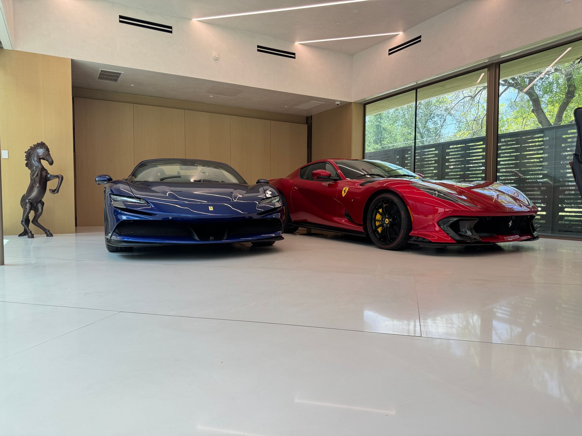 Two luxury sports cars in a modern garage: blue McLaren, red Ferrari. Shiny white floor, large windows.