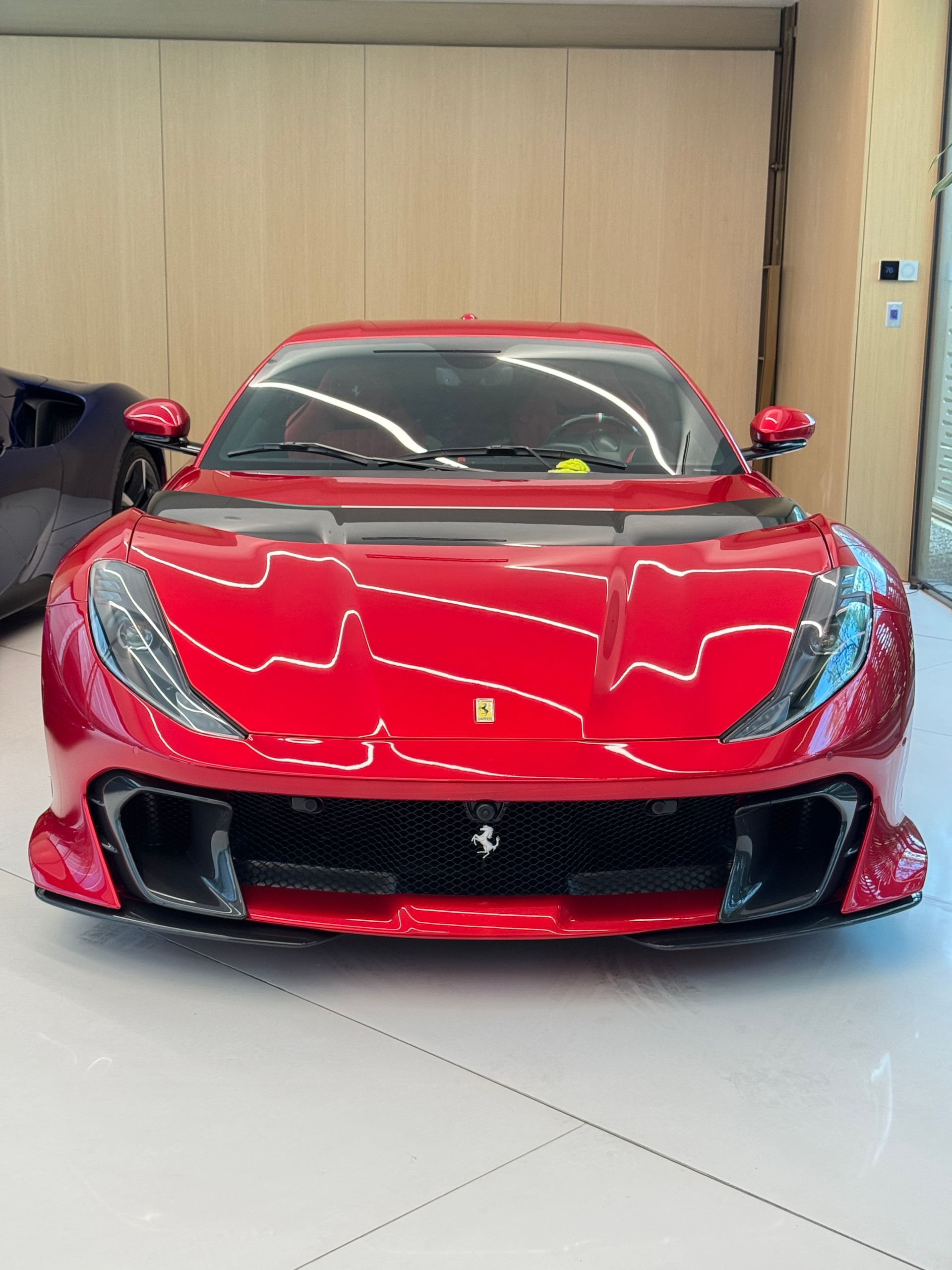 Red Ferrari sports car parked indoors, reflecting on a white floor.