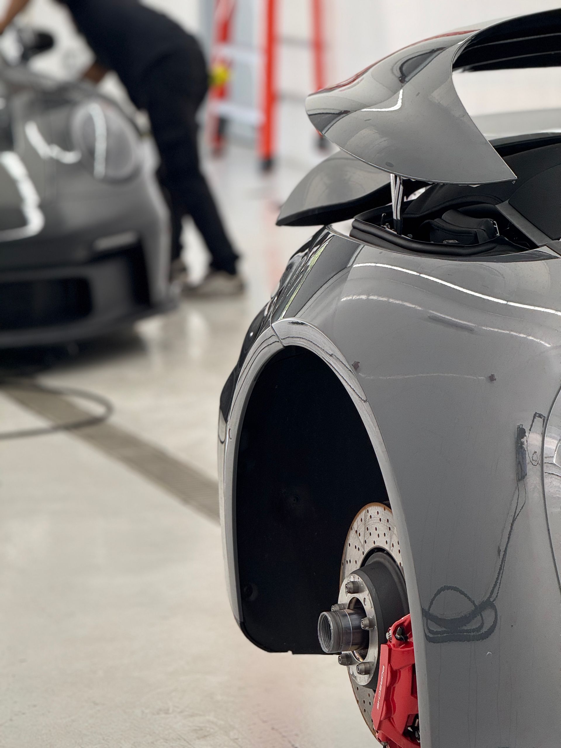 Gray sports car with open hood, red brake calipers. Mechanic in background.