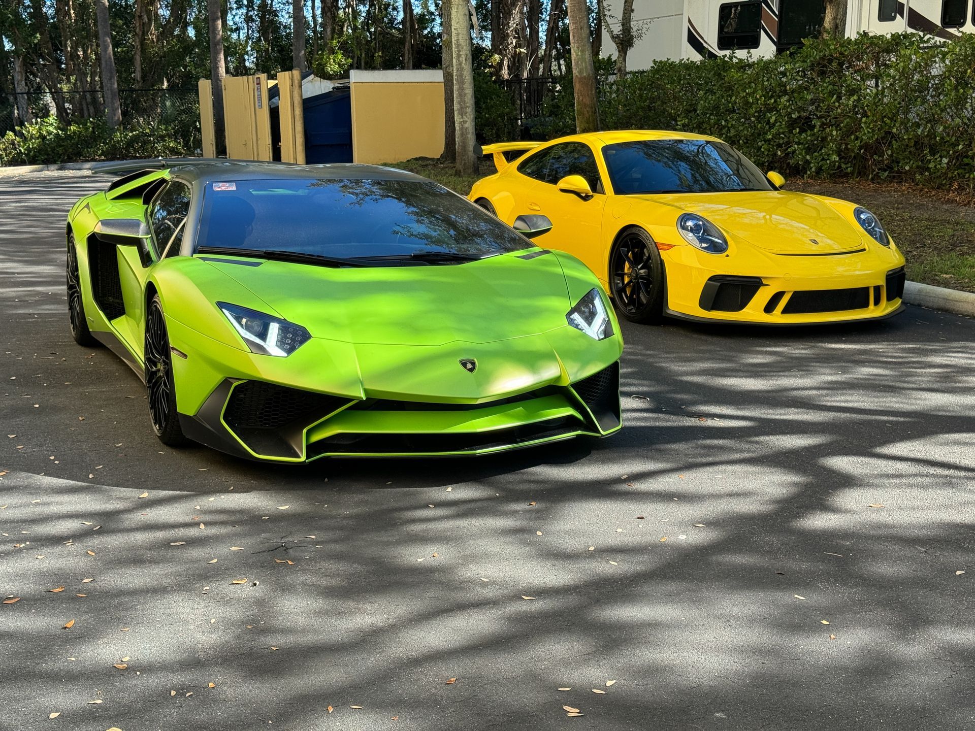 Lime green Lamborghini and yellow Porsche parked on a paved road.