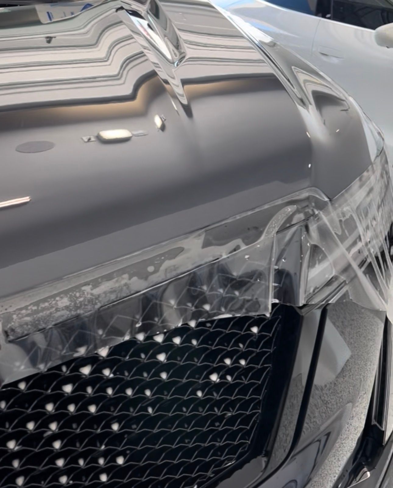 Black car hood with clear protective film over the front, near a black grill.