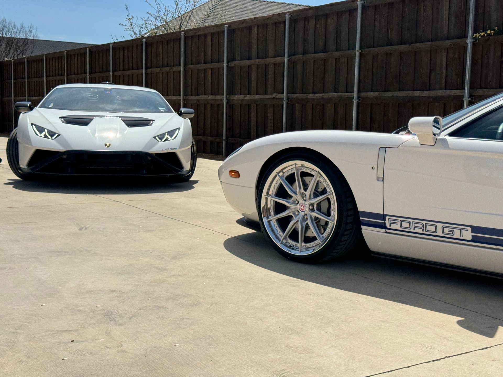 White Lamborghini and Ford GT parked side-by-side in front of a wooden fence.