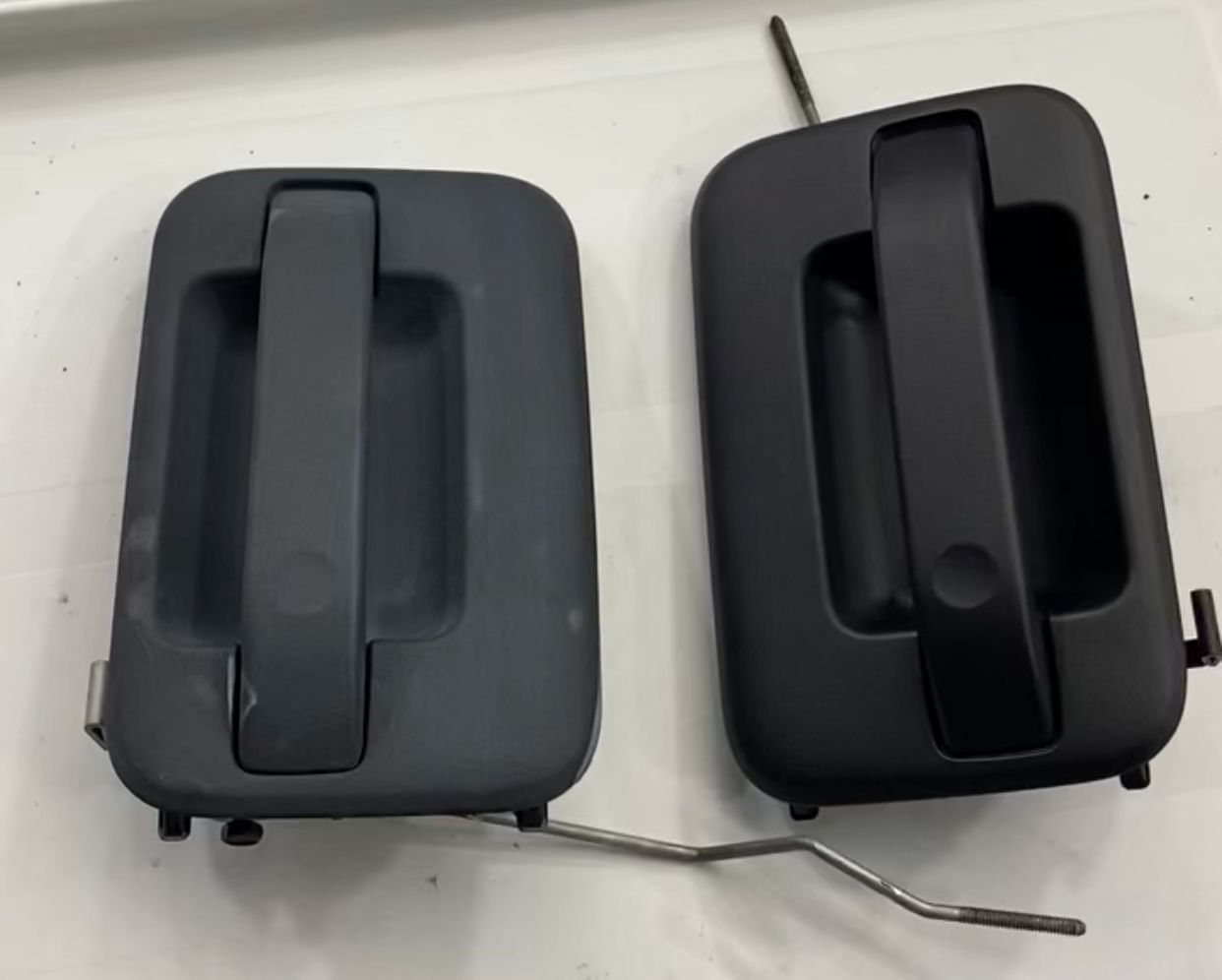 Two black exterior door handles with metal rods against a white surface.