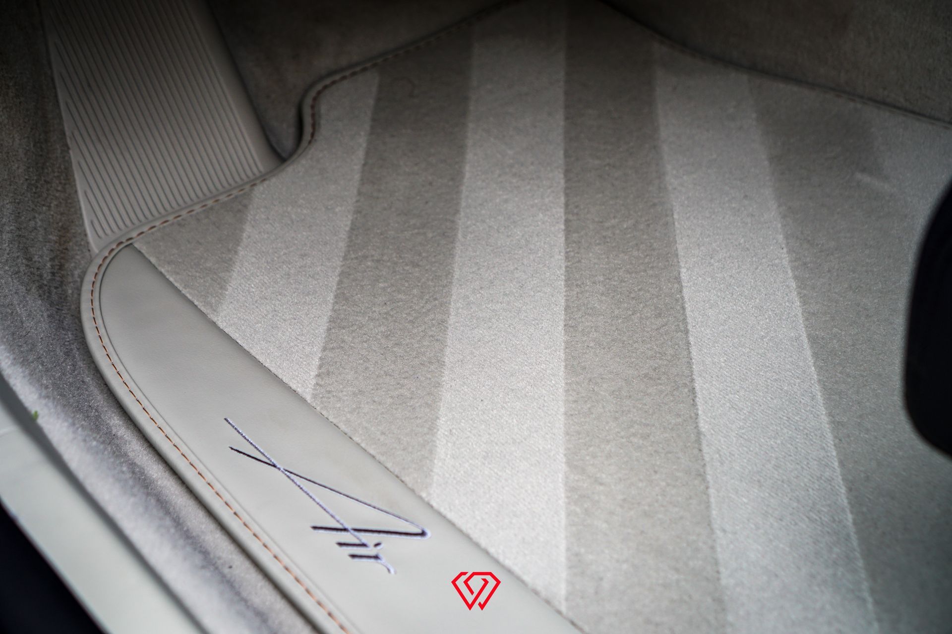 Beige car floor mat with striped pattern and logo.