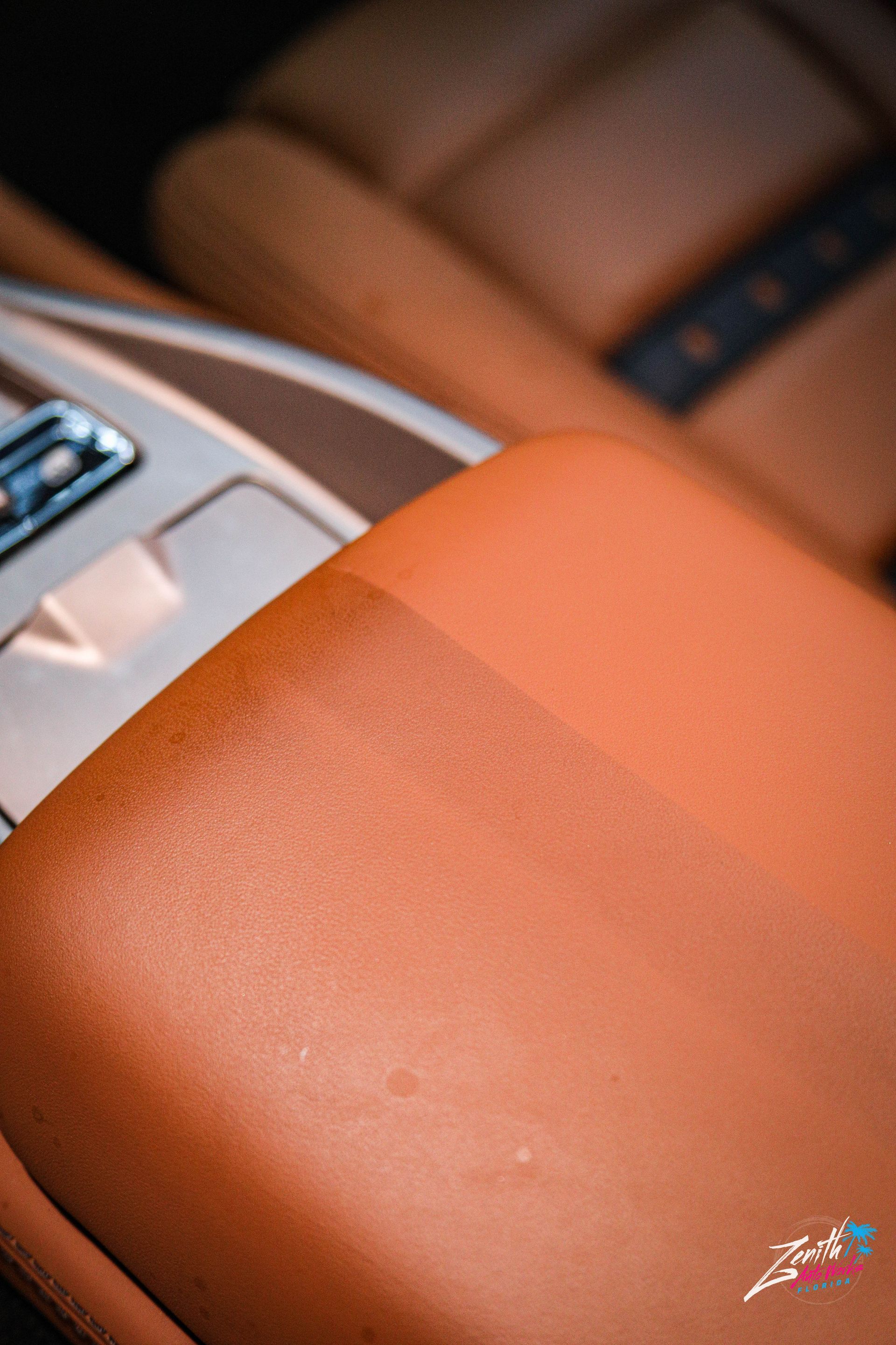 Close-up of a tan leather car interior. Armrest and seats visible, silver console details.