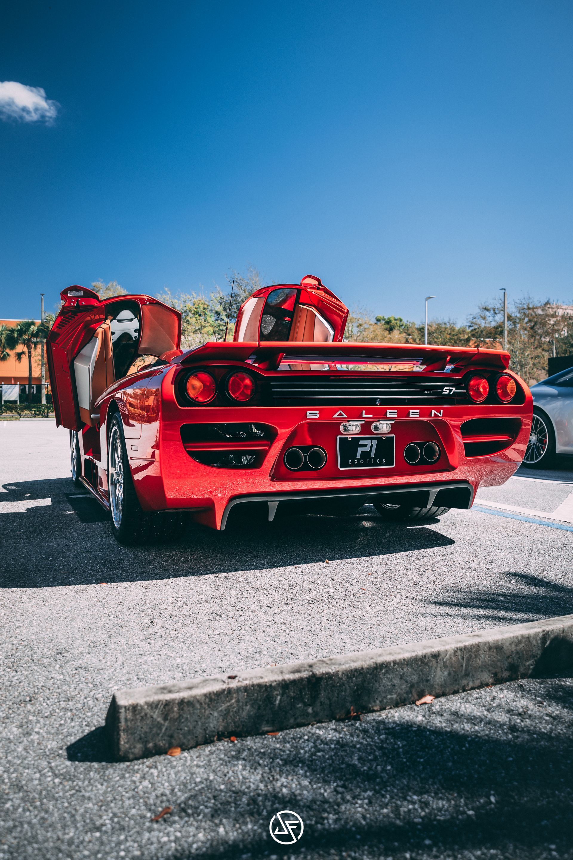 Red Lamborghini Diablo with doors open, parked on asphalt under a blue sky.