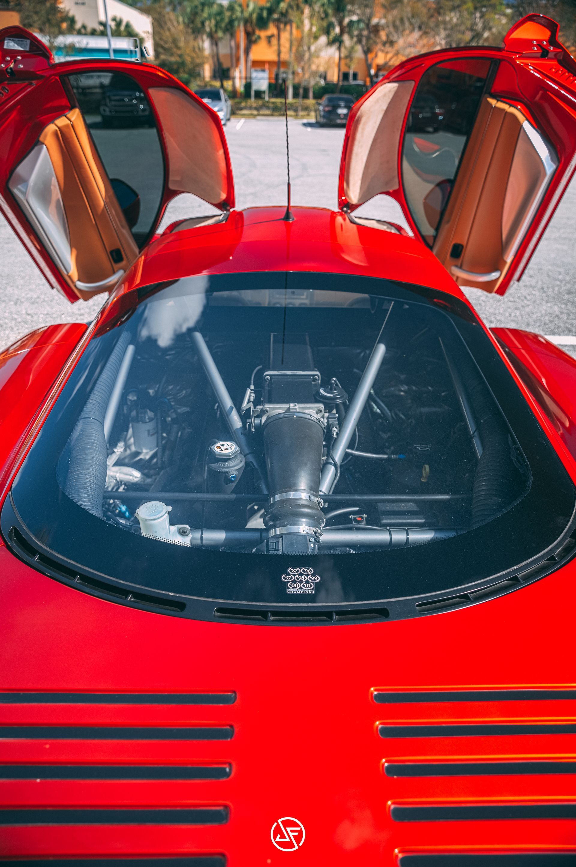 Red sports car with gull-wing doors open, revealing the engine.