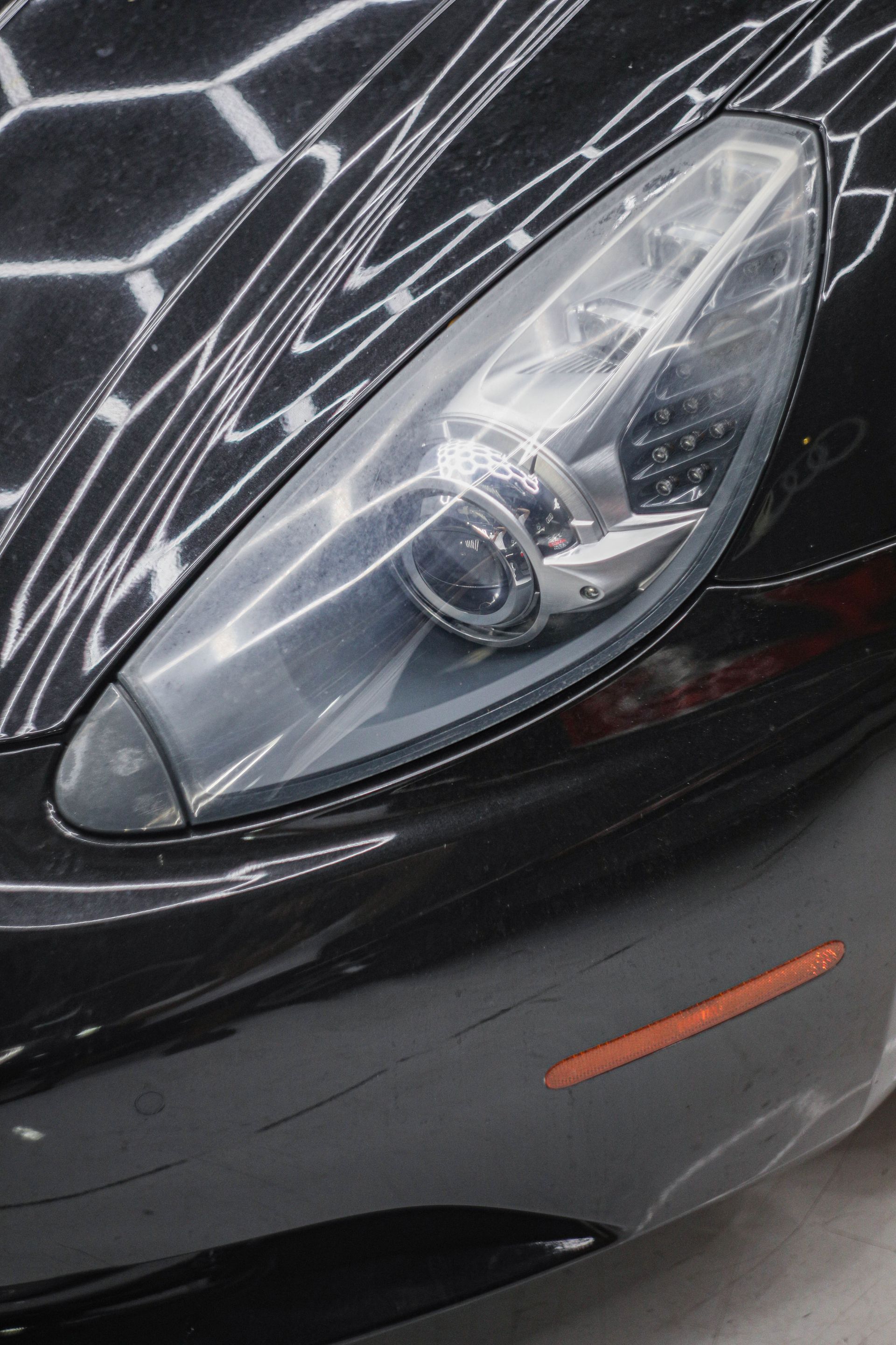 Close-up of a black sports car headlight. The shiny surface reflects overhead lights.