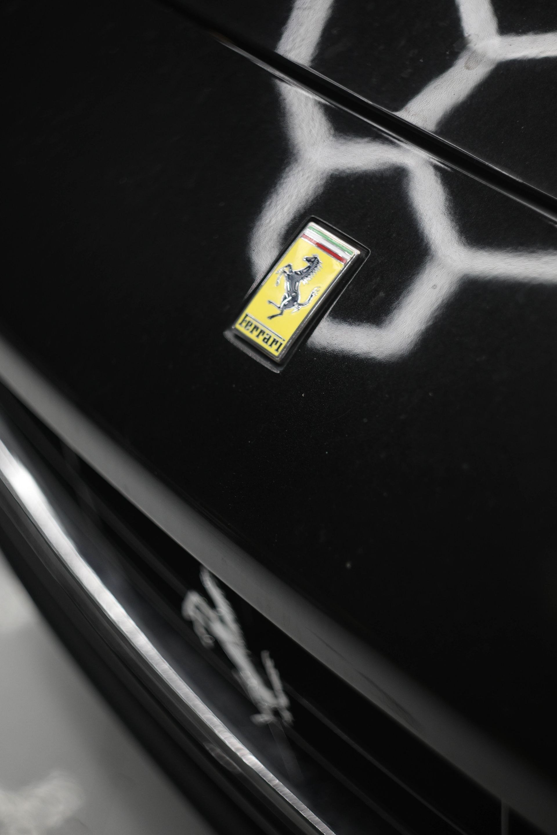 Black Ferrari hood with yellow and black emblem; honeycomb light reflection.