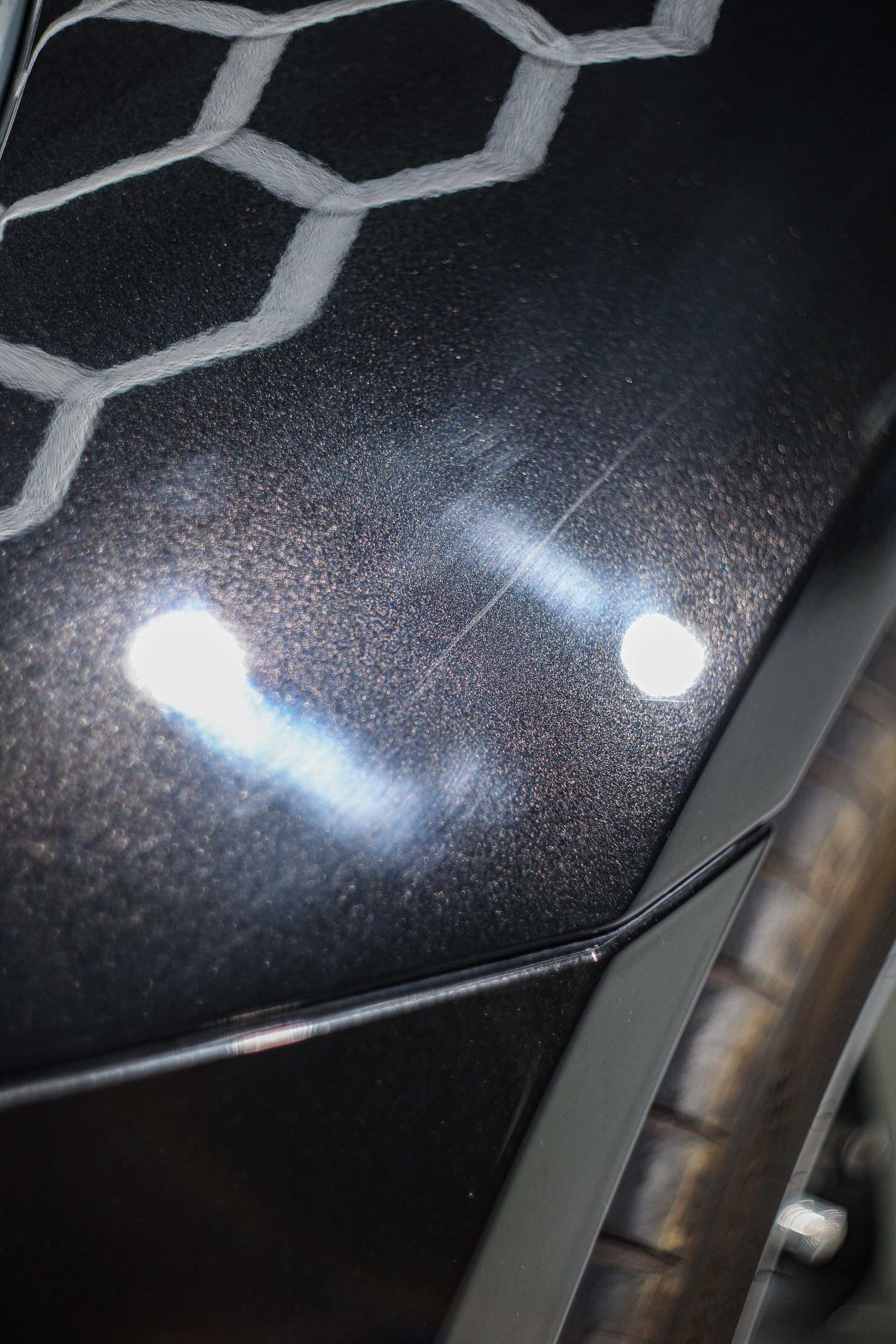 Close-up of a black car's body with a hexagonal pattern and light reflections.