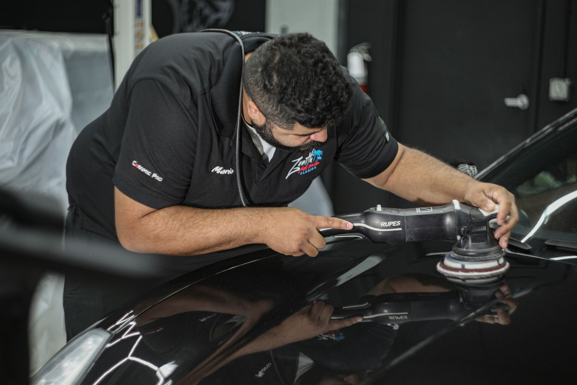 Man polishing a black car with a machine in a workshop.