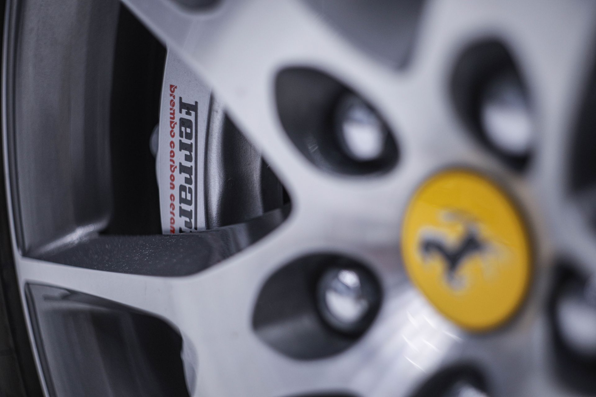 Close-up of a silver Ferrari wheel. Yellow emblem, red Ferrari brake caliper visible behind the spokes.