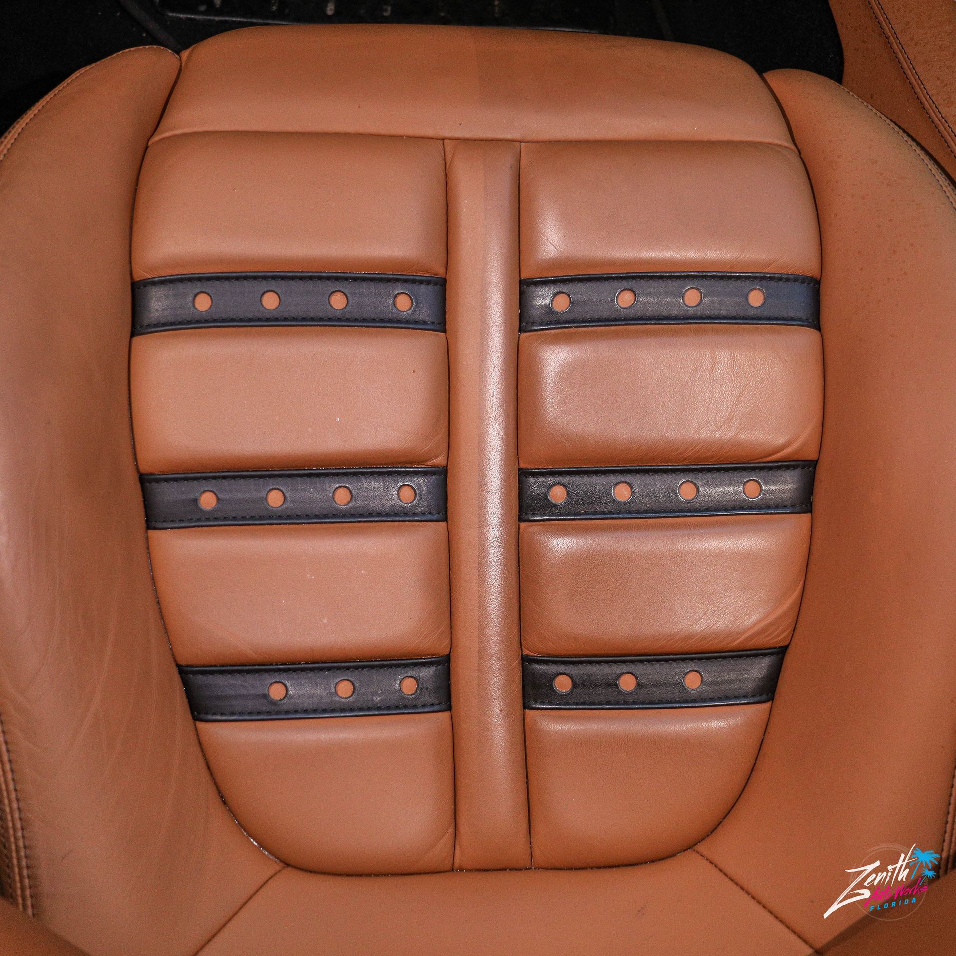Tan leather car seat with black accents and stitching.