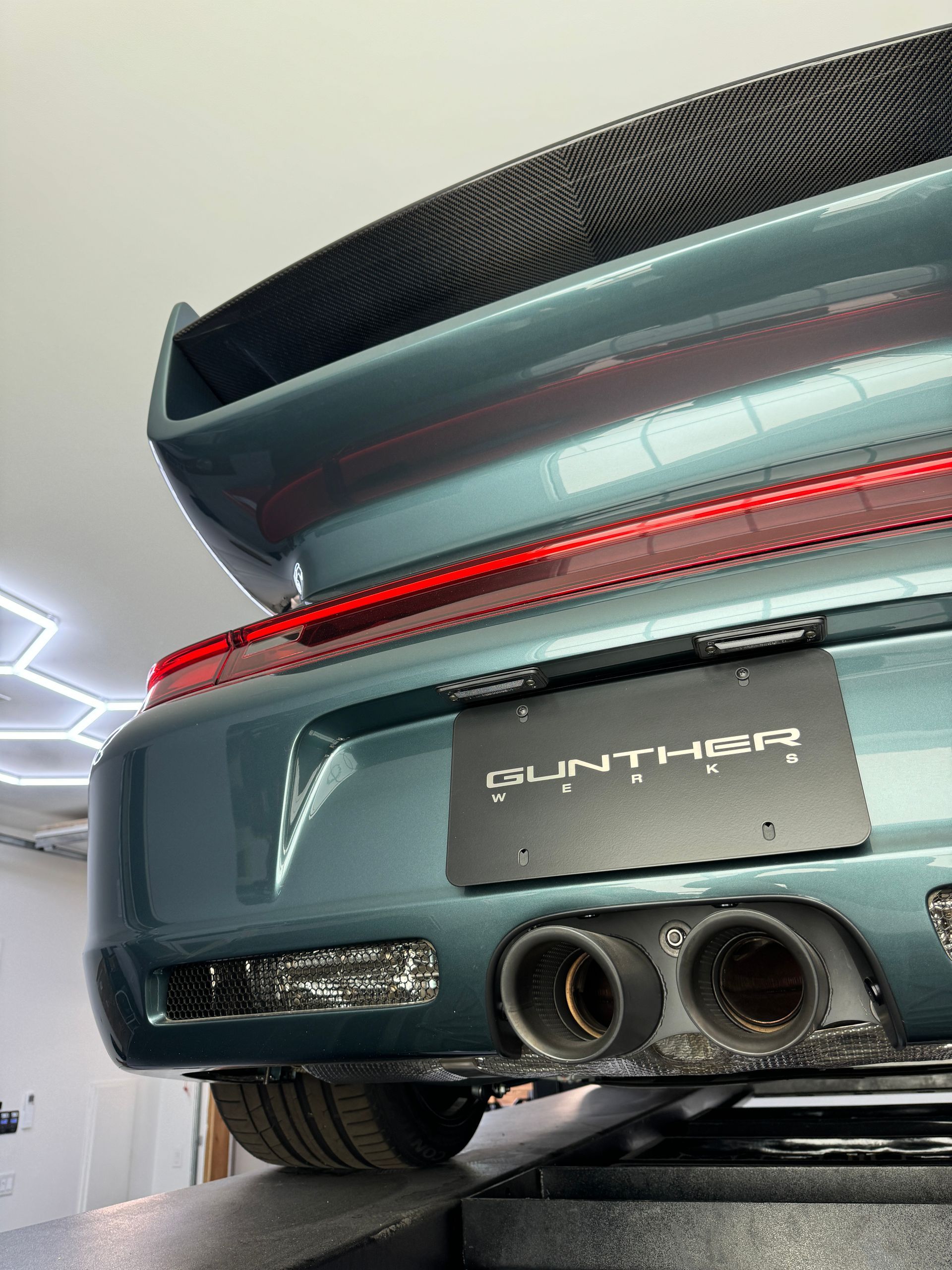 Rear view of a teal Porsche sports car with a large spoiler and dual exhaust.