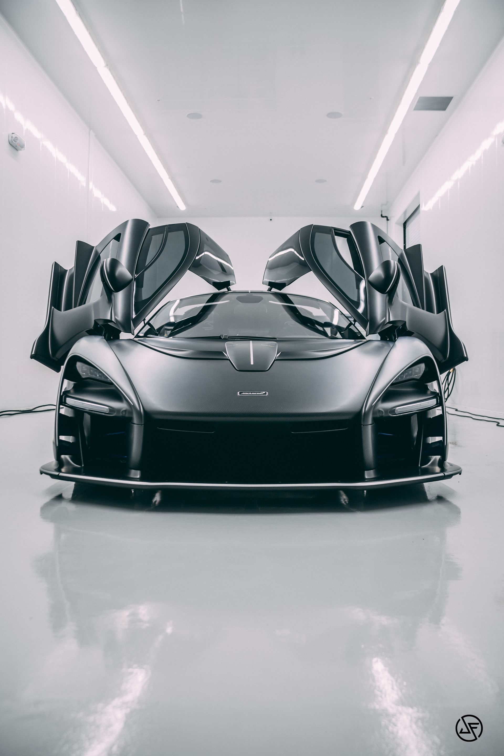 Black McLaren Senna with doors open, in a bright, modern garage.
