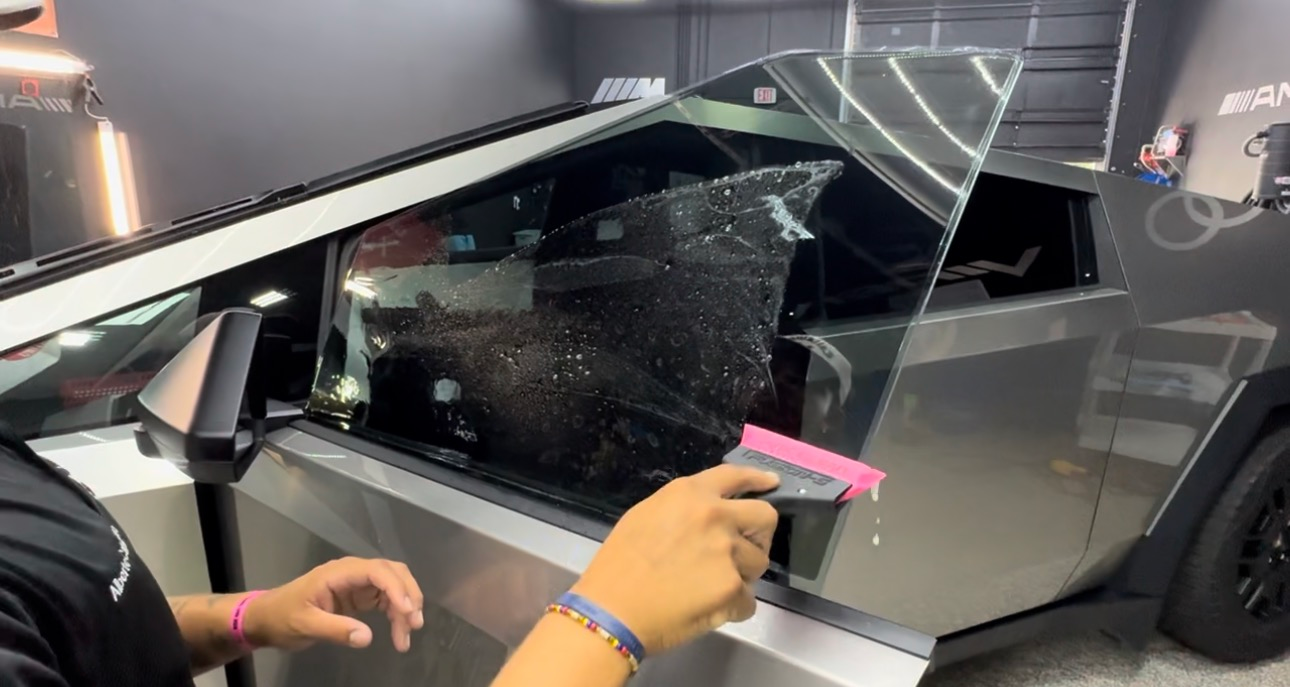 A person applying tint to a Tesla Cybertruck window with a squeegee in a shop.