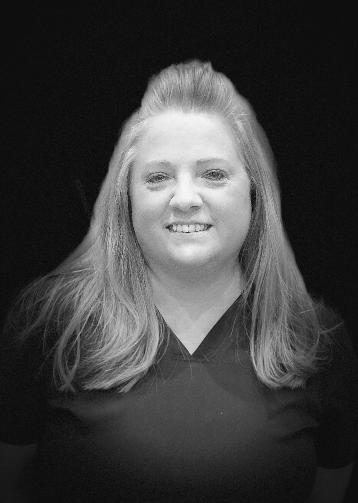 A black and white photo of a woman wearing a scrub top and smiling.
