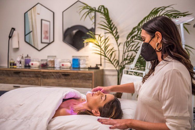 A woman wearing a mask is giving a massage to a woman laying on a bed.
