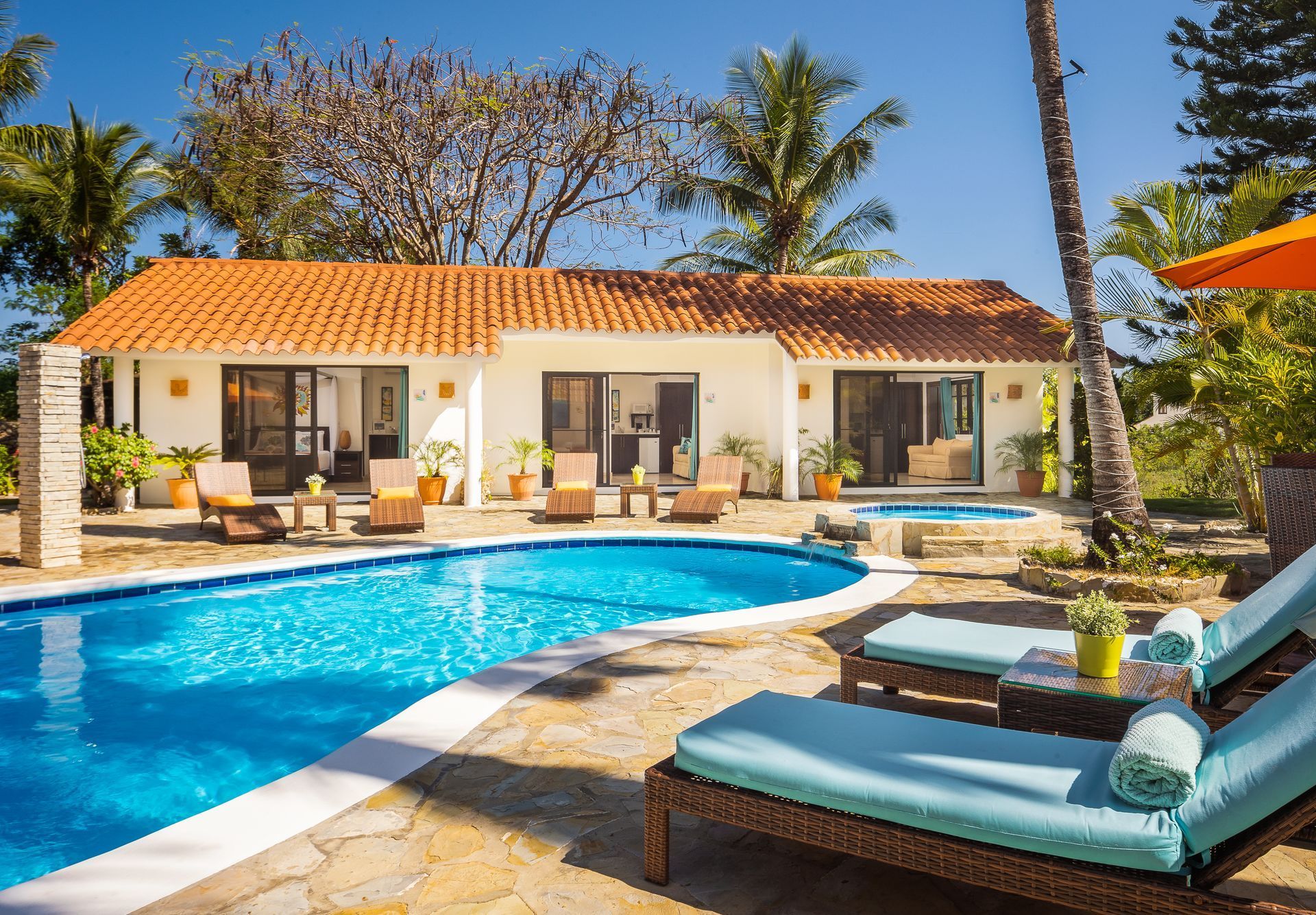 Luxurious tropical triplex with pool, terracotta roof, and lounge chairs under a sunny sky.