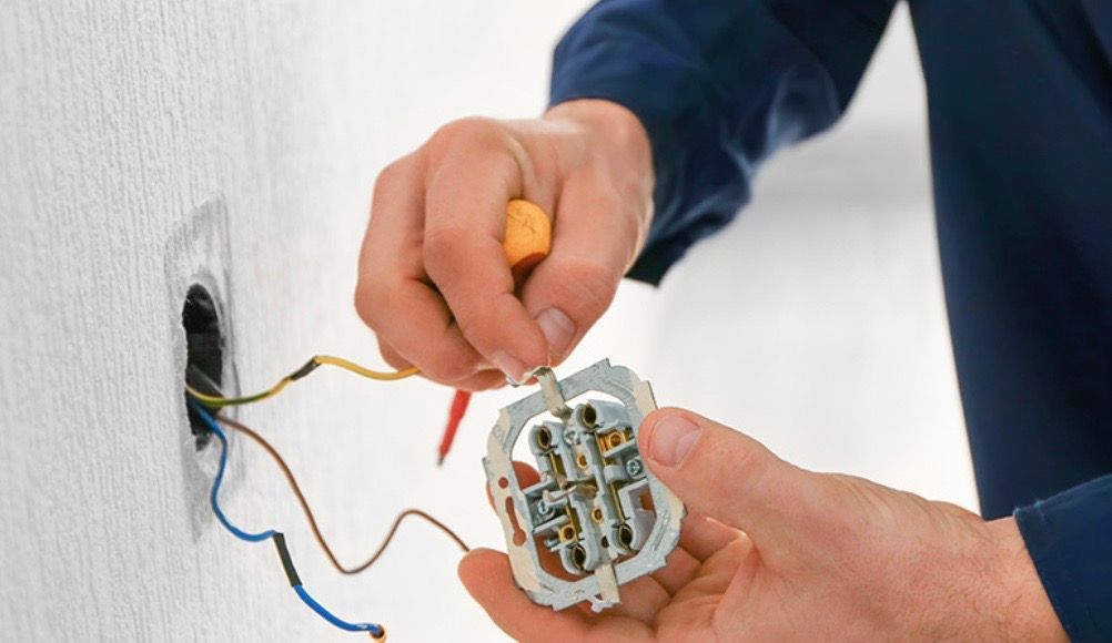 Electrician wiring a wall outlet, holding a screwdriver.
