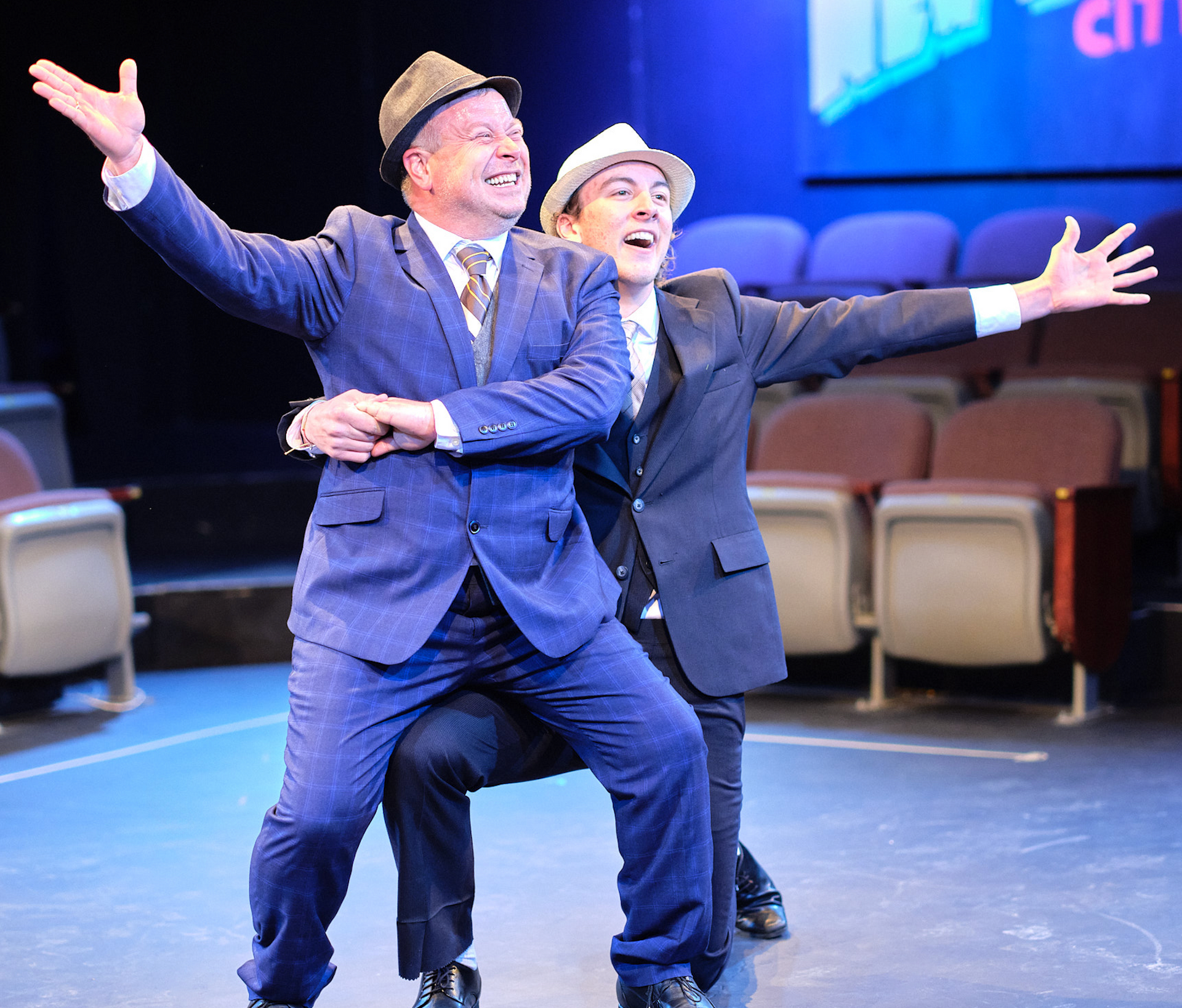 Two men in suits and hats are dancing on a stage