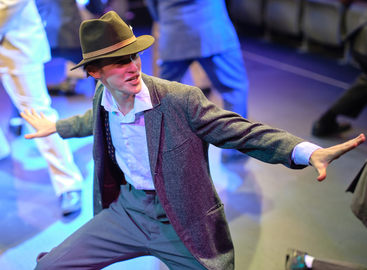 A man in a suit and hat is dancing on a stage