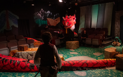 A man is standing in front of a large red snake on a stage.