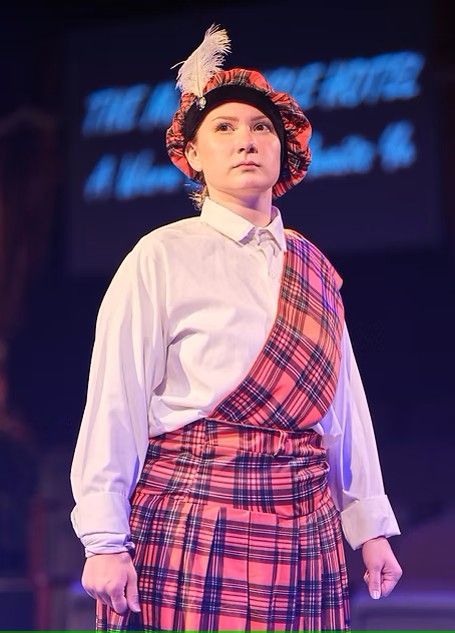 A woman in a kilt and hat is standing on a stage