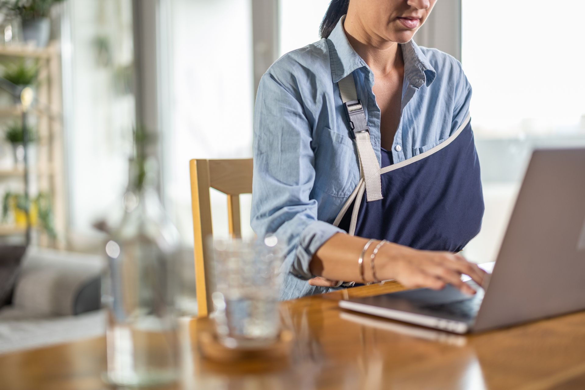 A woman with a broken arm is sitting at a table using a laptop computer.