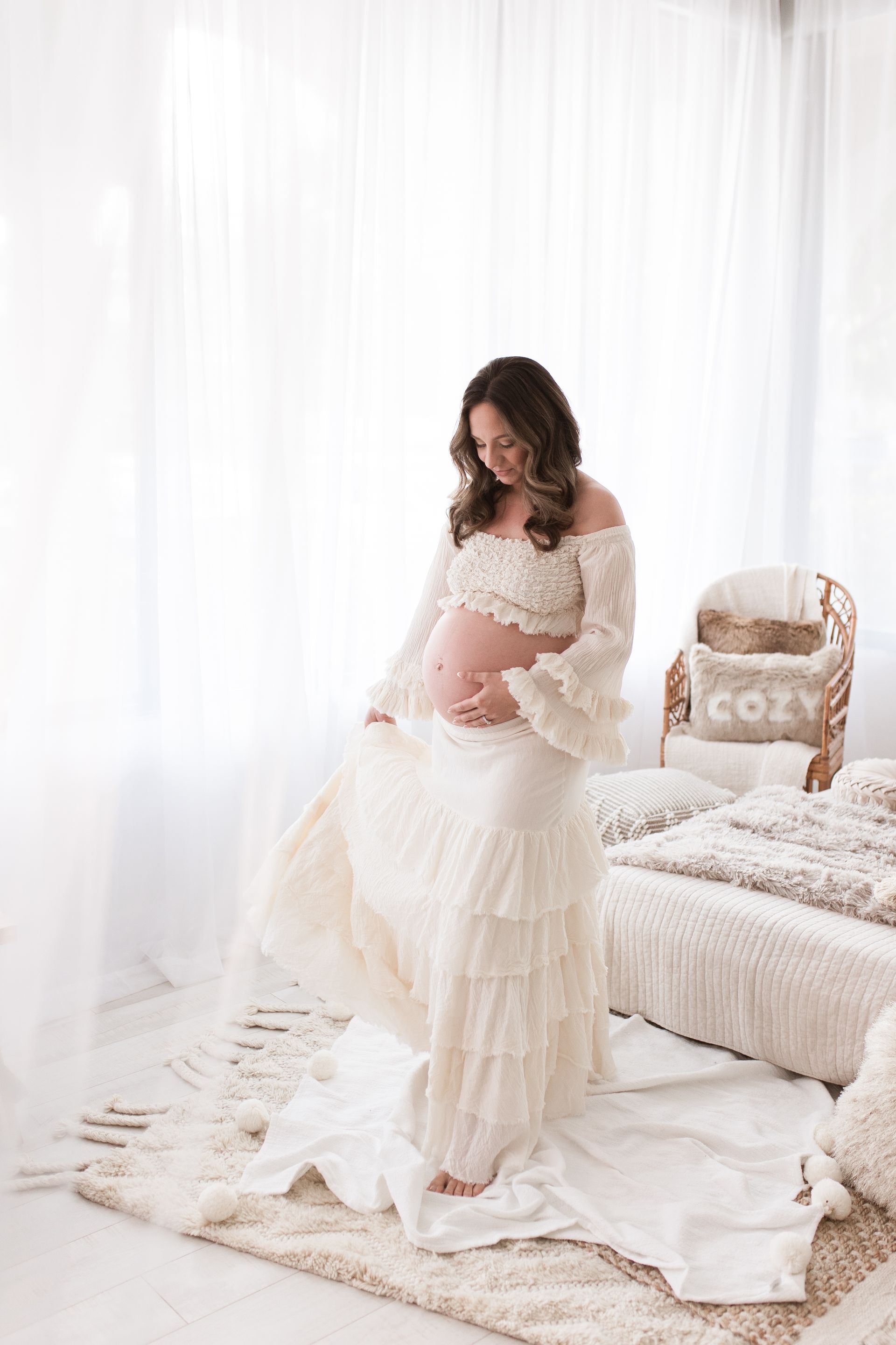 A pregnant woman in a lace dress is standing on a white background.