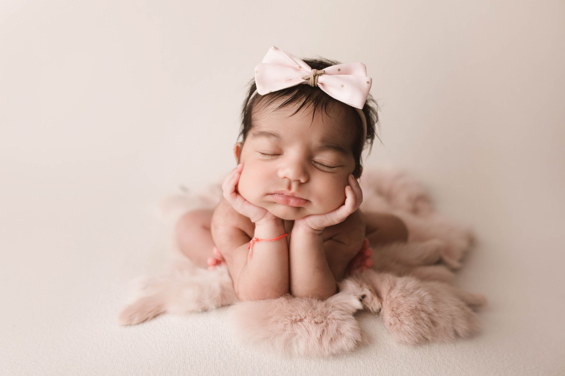 A newborn baby wearing a white hat is sleeping on a white blanket.