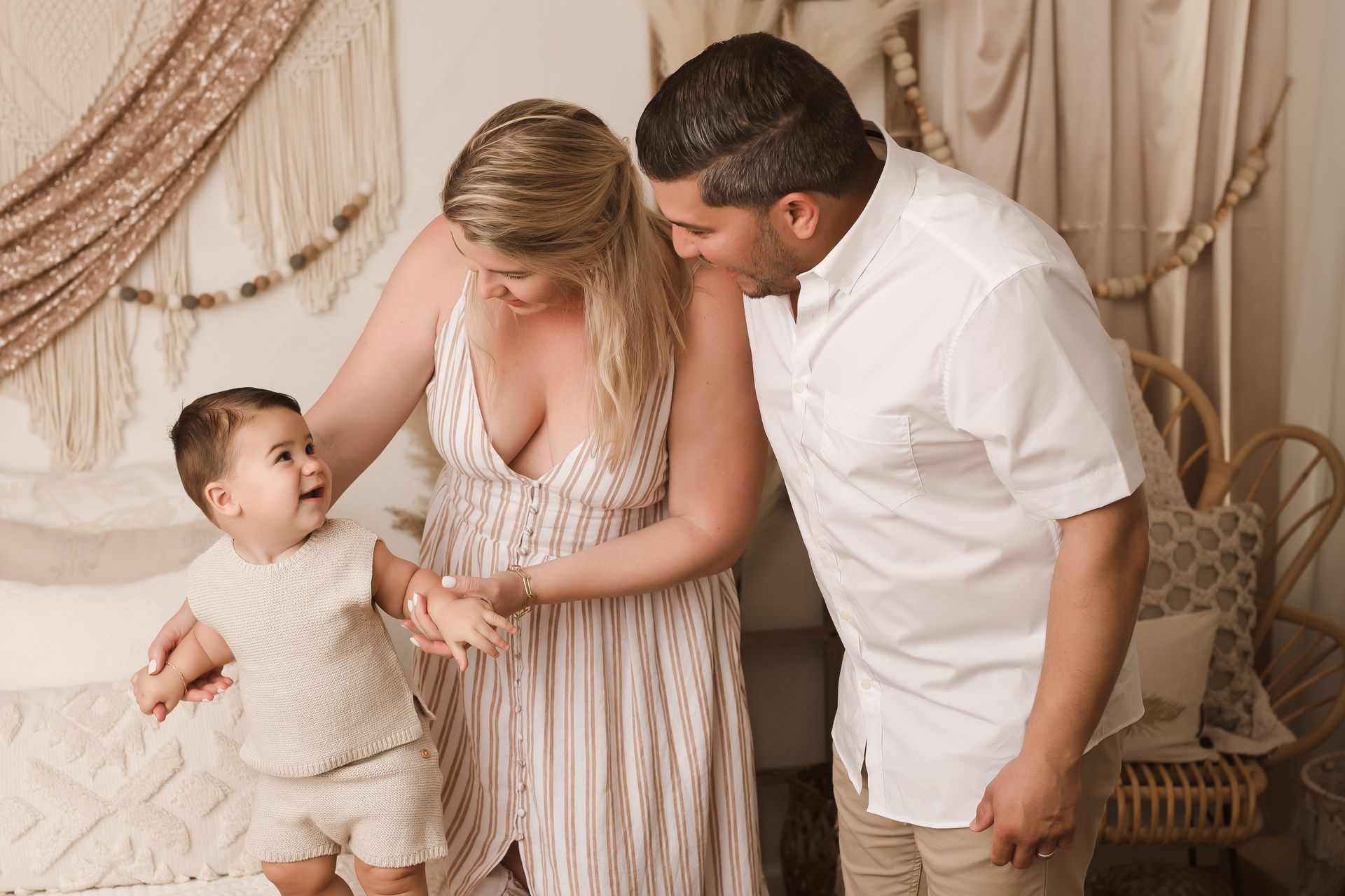 A man and a pregnant woman are standing on the beach holding hands.