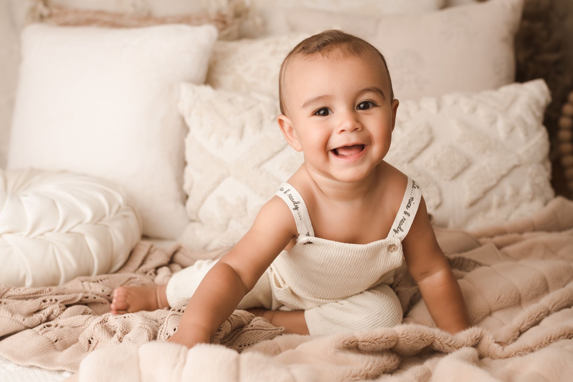 A baby is sitting on a chair and smiling at the camera.