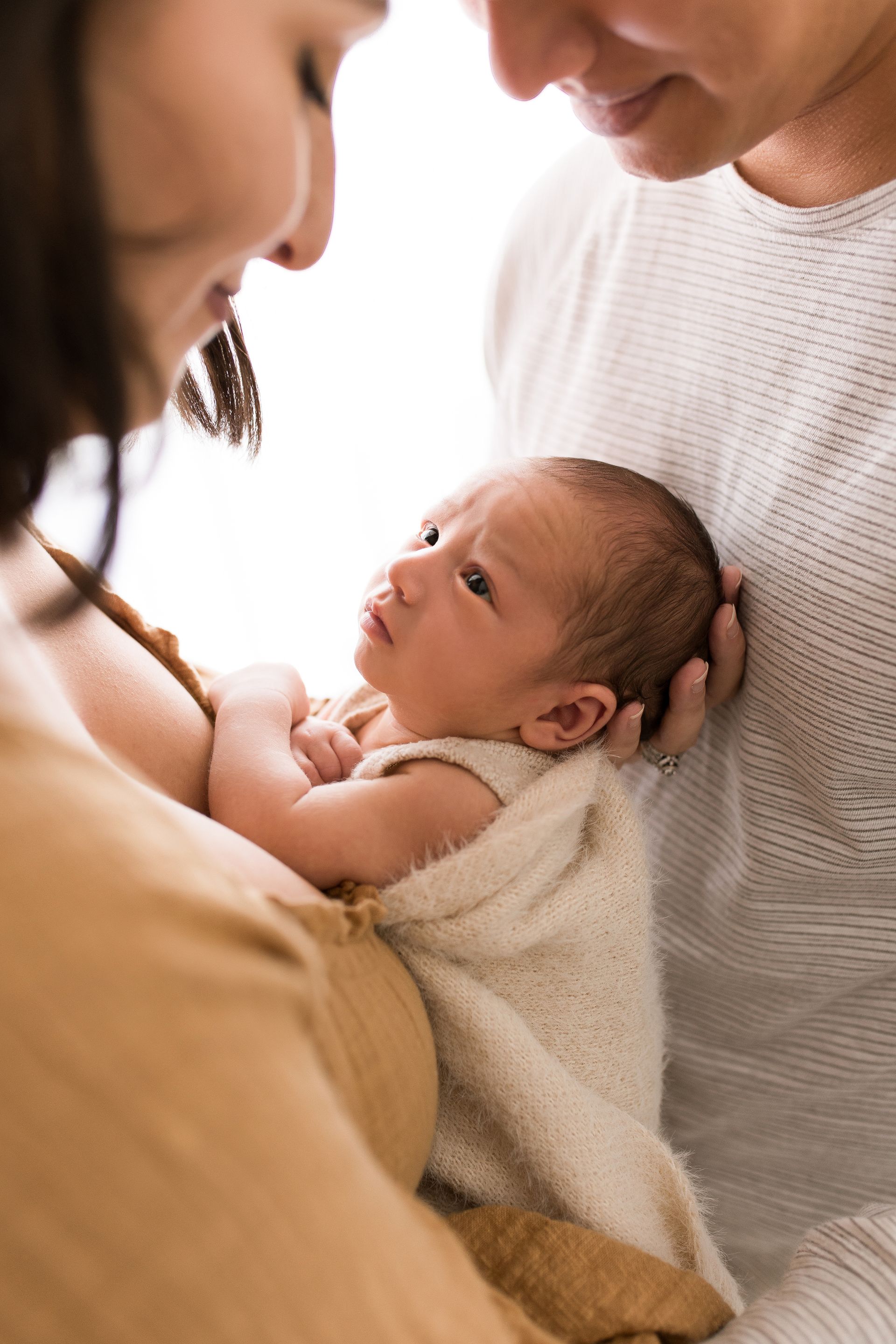 A baby wearing a white hat and sweater is laying on a white blanket.