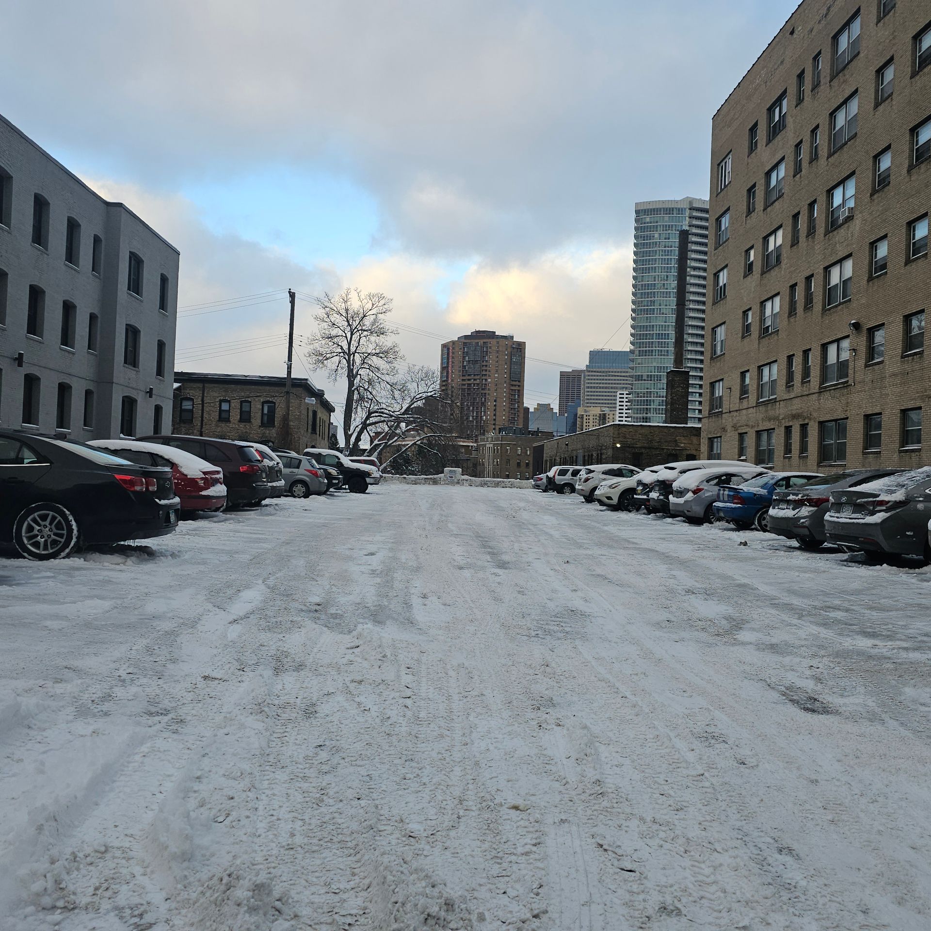 A snowy parking lot with cars parked in front of buildings