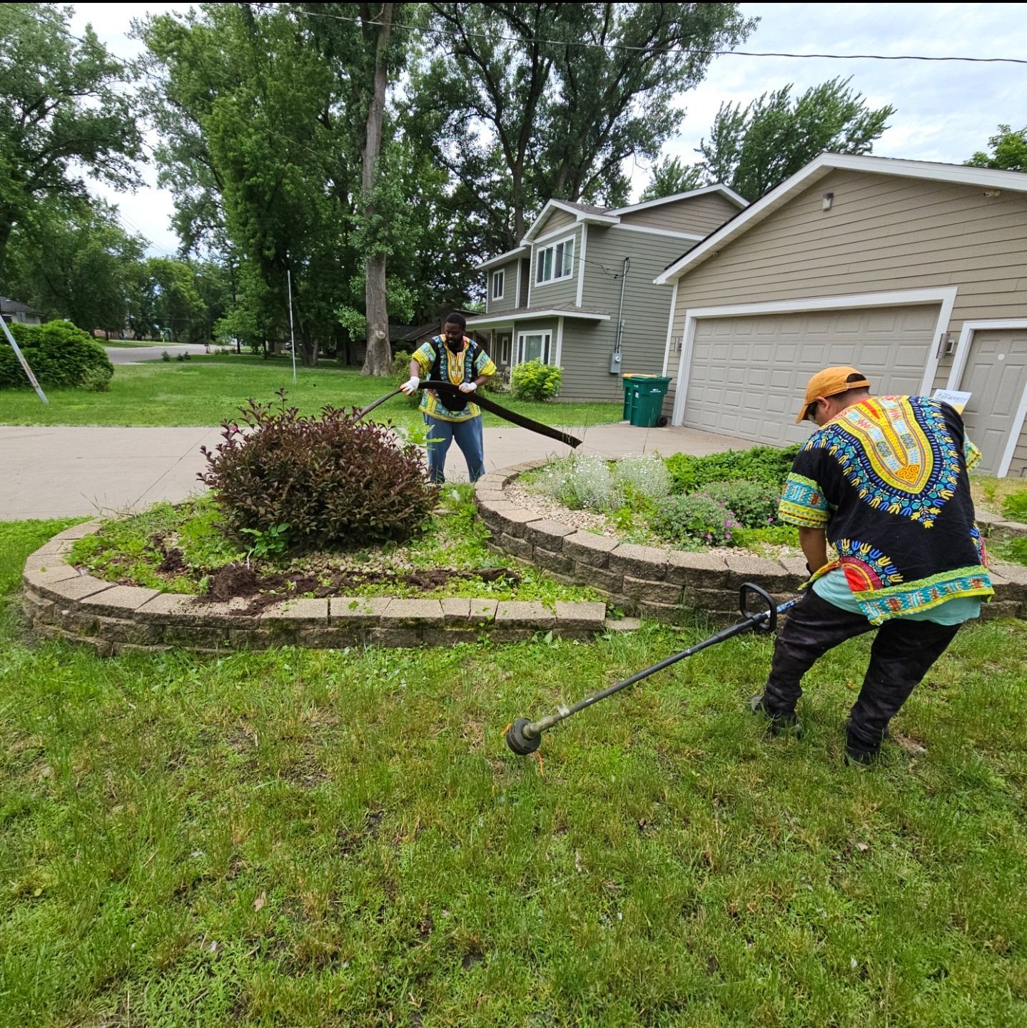 Two men are mowing a lawn in front of a house