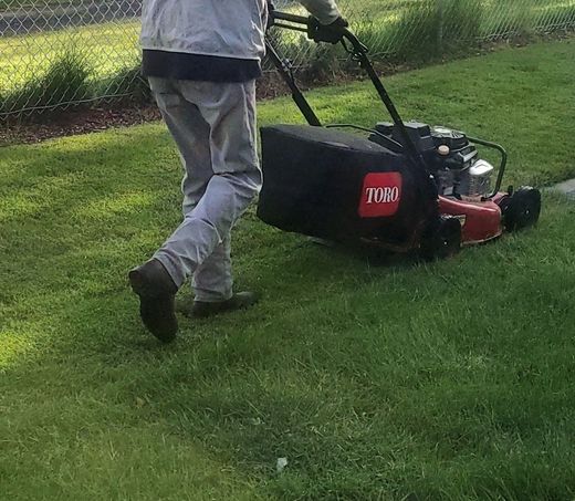 Person in apron and gloves standing beside a black lawn mower on a white background