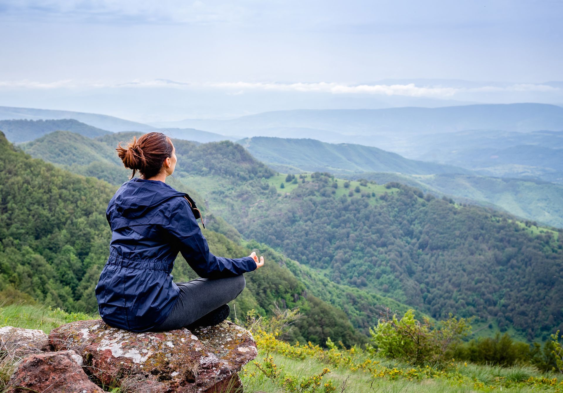 A woman is sitting on a rock on top of a mountain meditating.