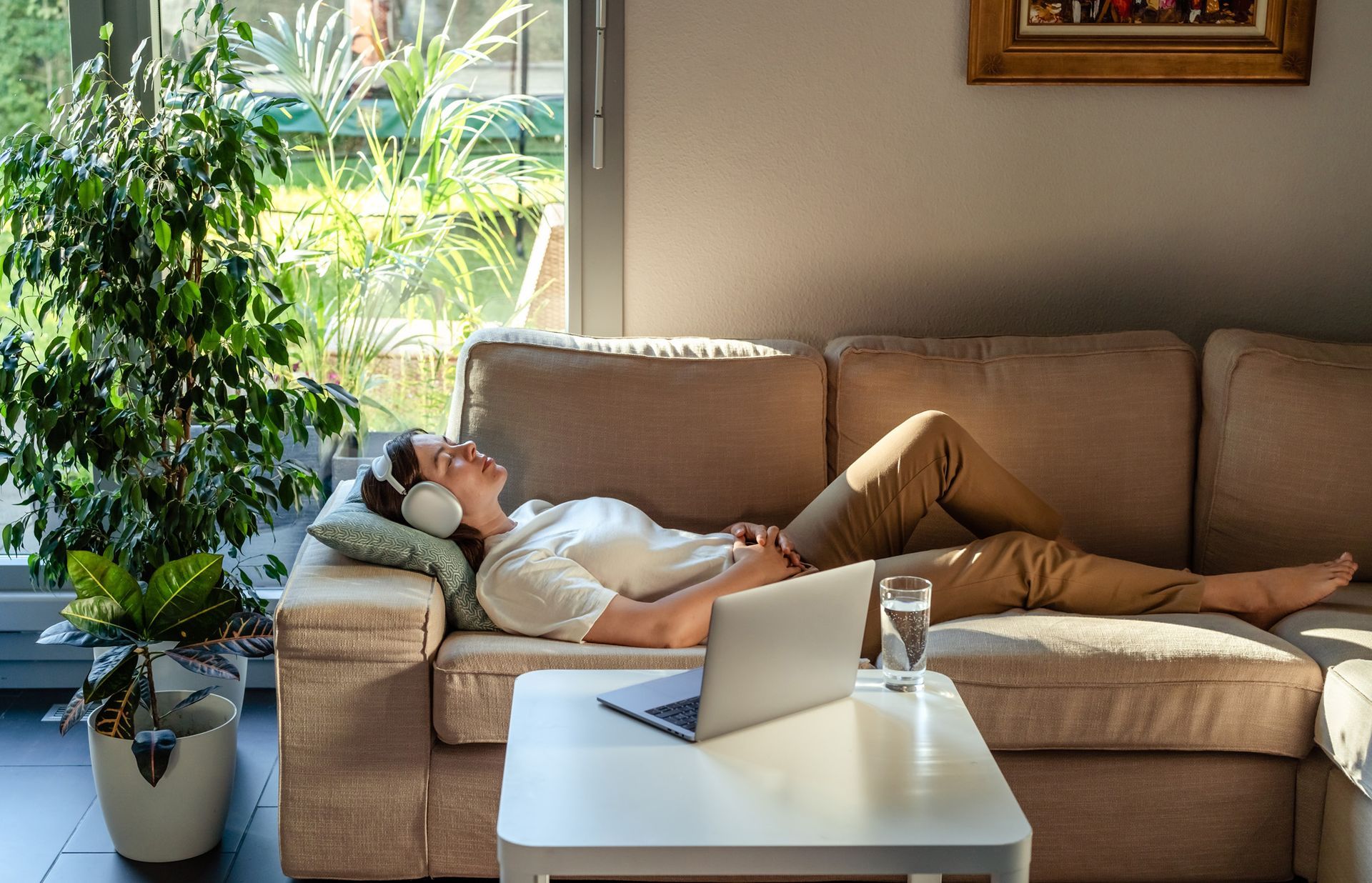 A woman is laying on a couch wearing headphones and listening to music.