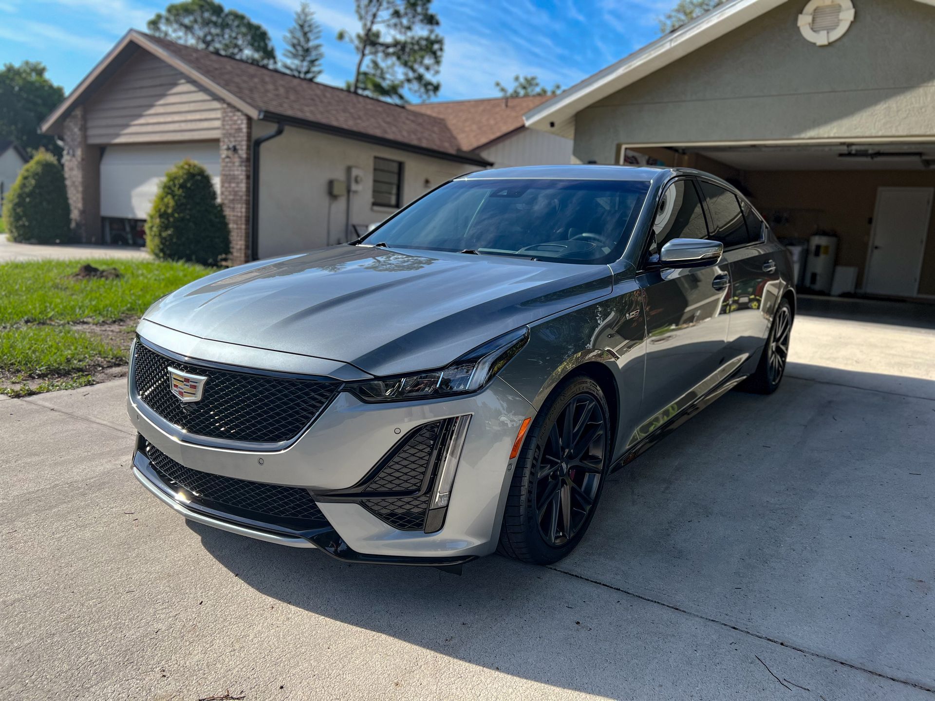 Silver Cadillac sedan parked in front of a house on a sunny day.