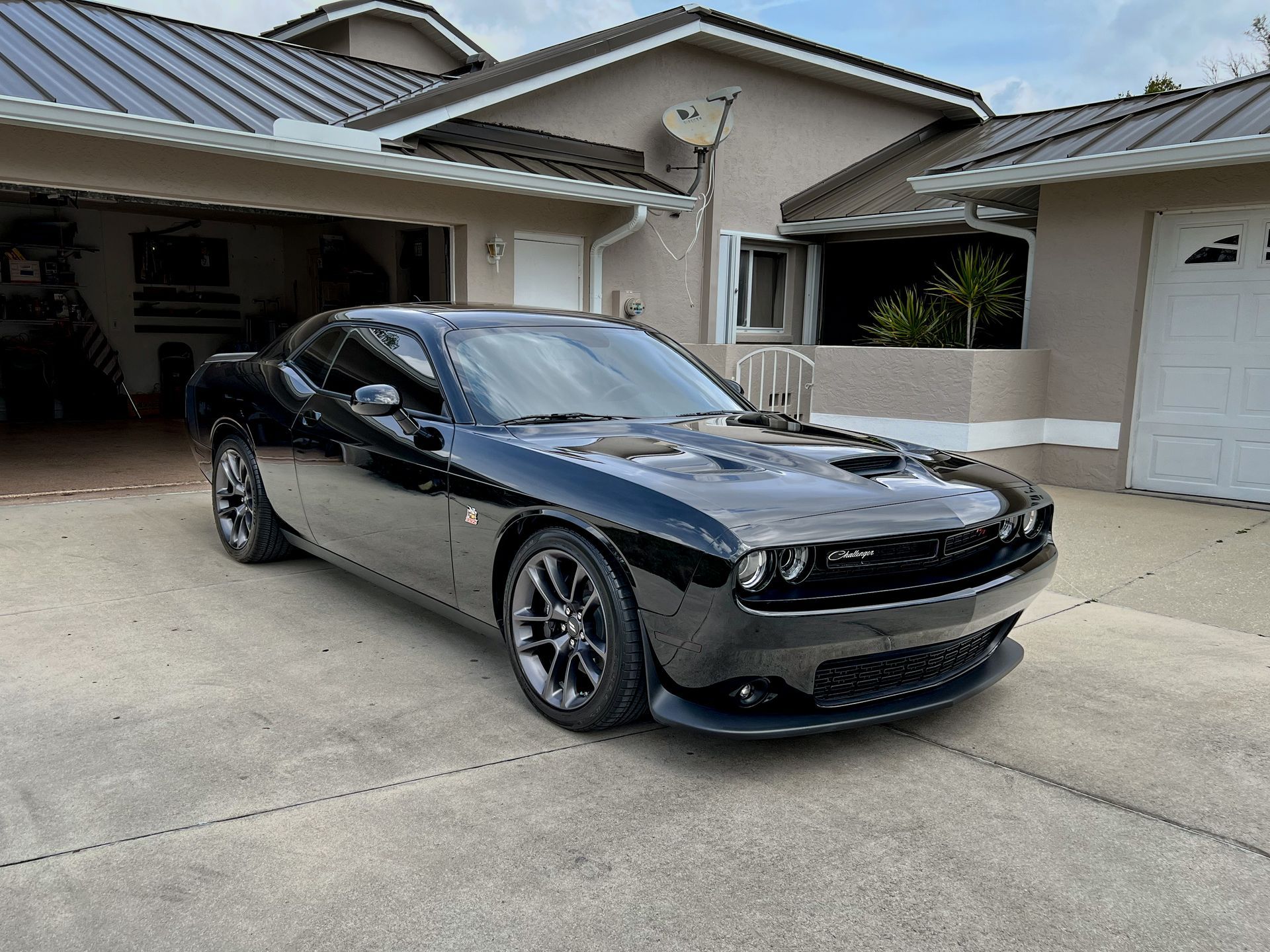 Black Dodge Challenger parked in front of a beige house with a driveway.