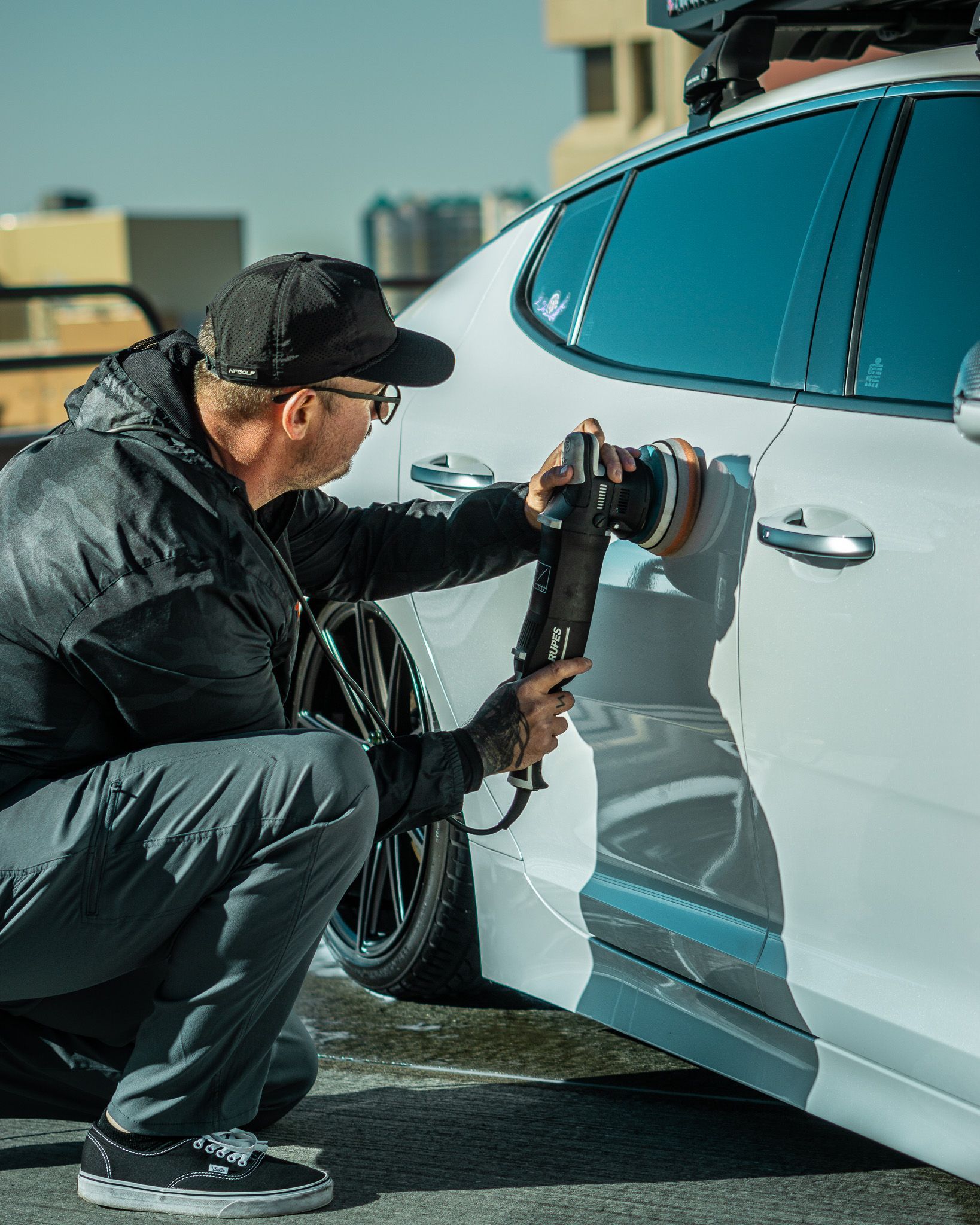 Man polishing a white car with a power buffer outdoors.