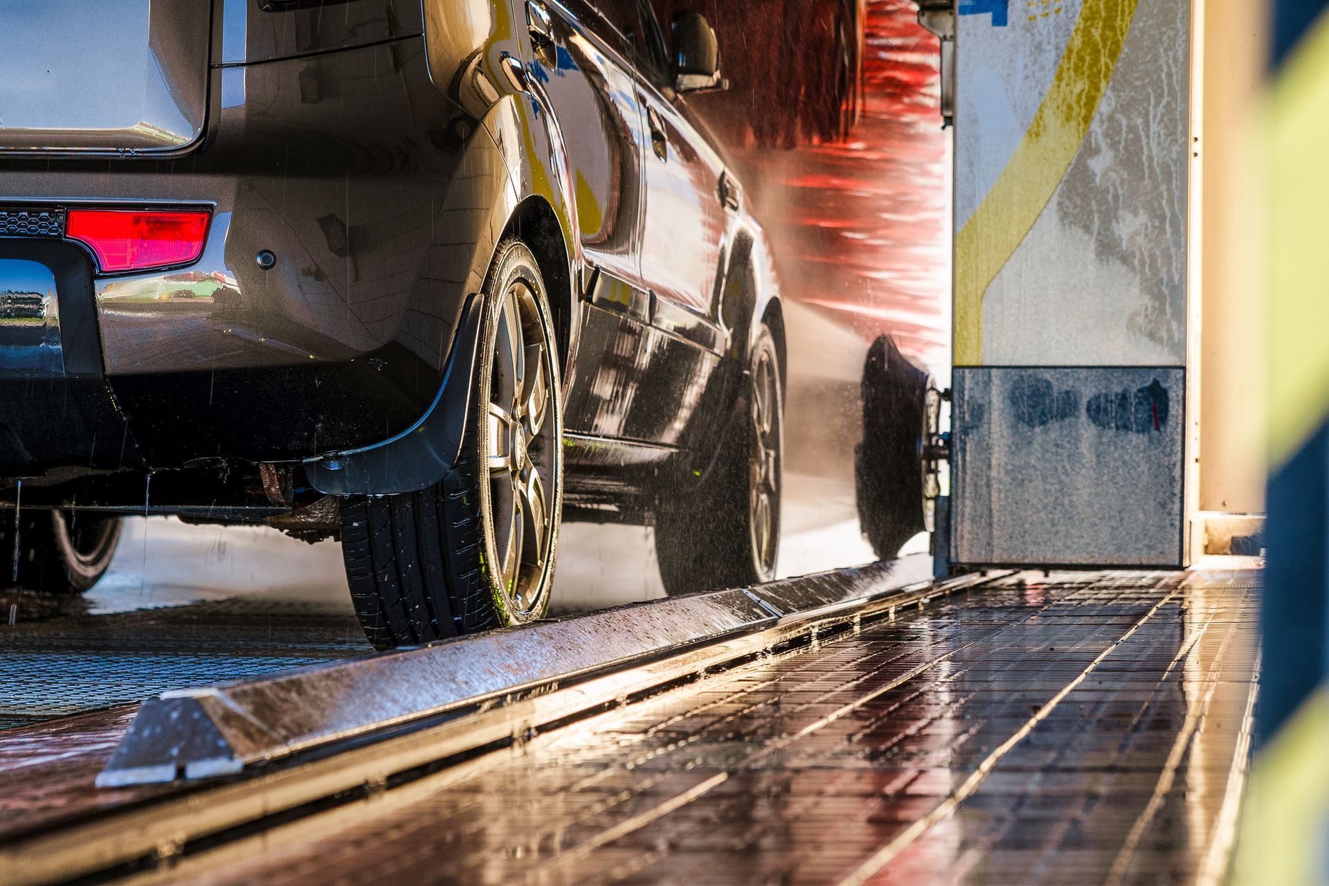 Car being washed in an automated car wash; water and brushes are visible.