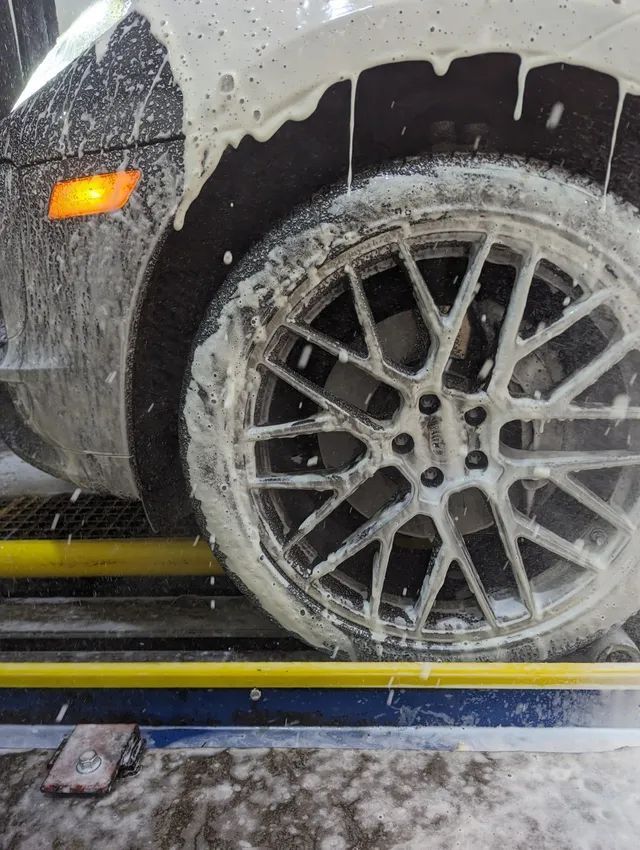 A car wheel covered in white soap suds at a car wash, with an orange blinker light on.