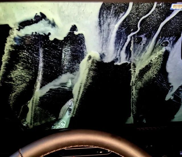 Inside a car during a car wash. Soap and water obscure the windshield, view from behind the steering wheel.