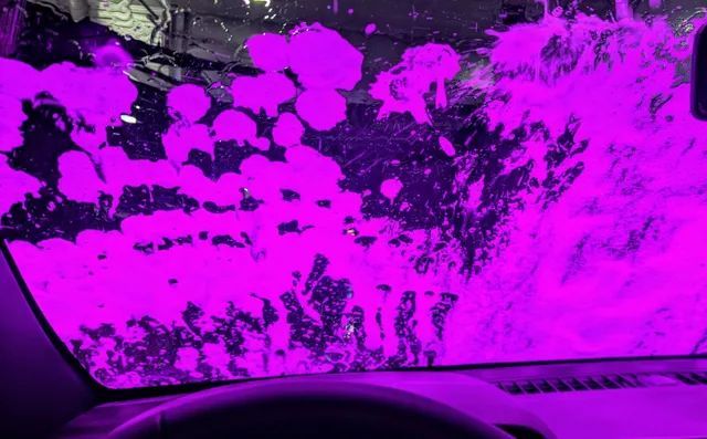Inside a car, windshield covered in vibrant purple soapy wash at a car wash.