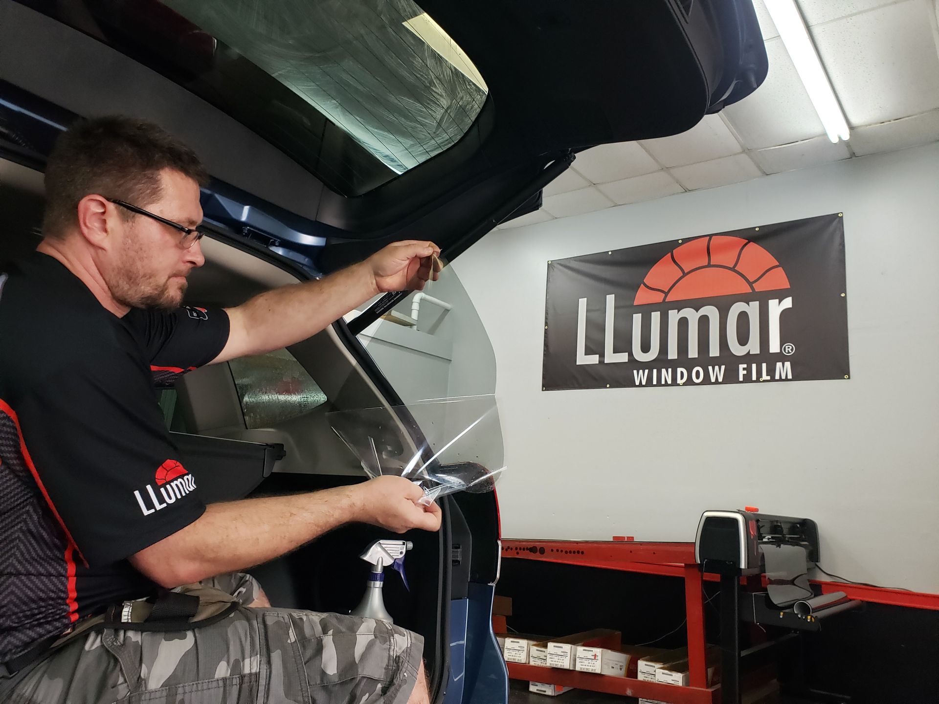 A man is installing window film on a car in a garage.