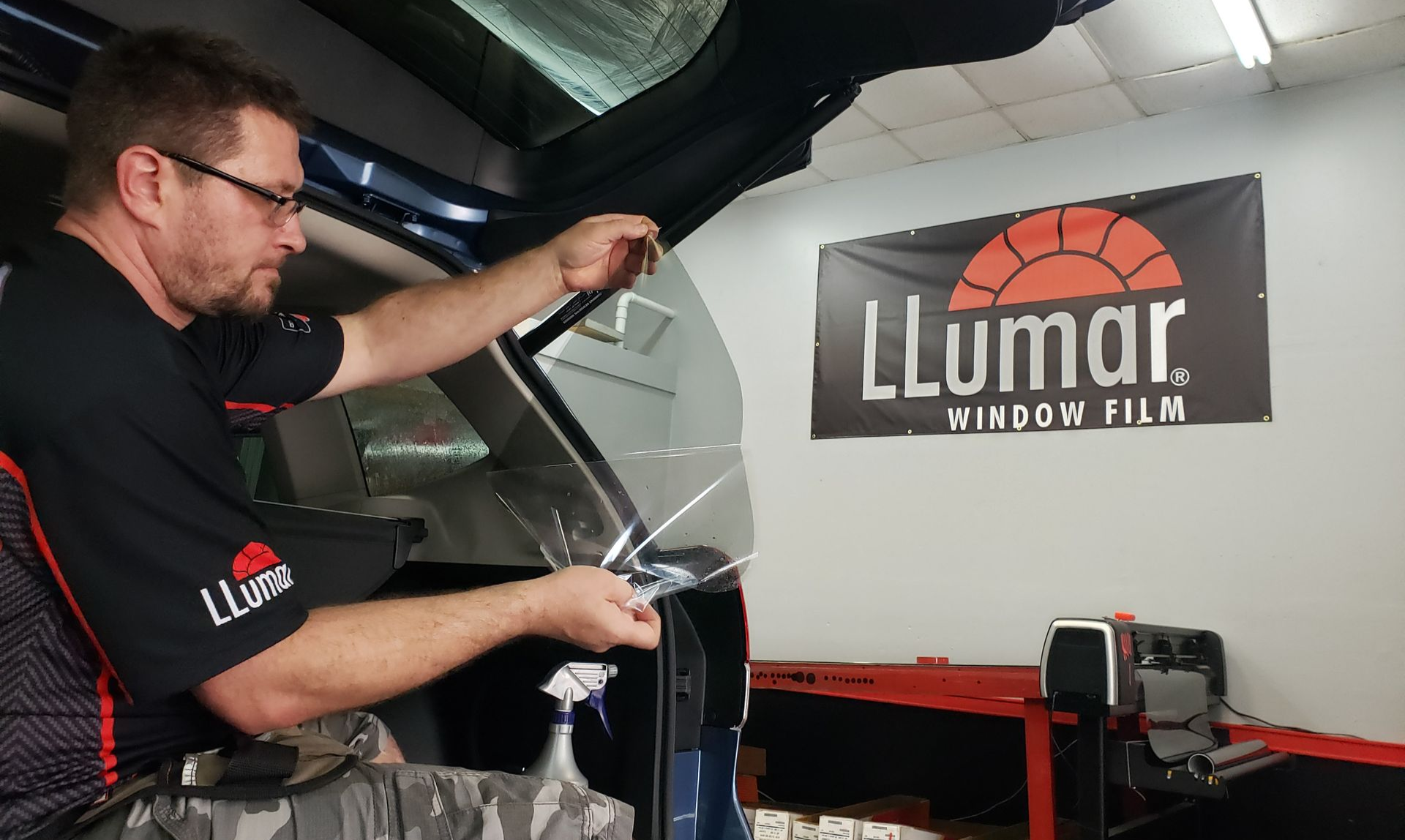 A person applying window film inside a vehicle, in front of an 